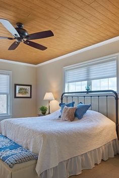 a bedroom with a bed, ceiling fan and two windows that have shades on them