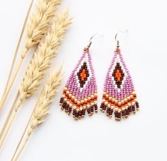 a pair of beaded earrings sitting on top of a table next to some dried grass