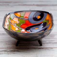 a colorful bowl sitting on top of a wooden table next to a white wall or floor