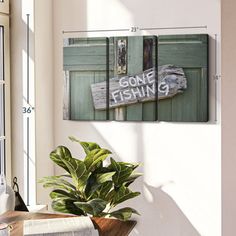 a wooden sign hanging on the side of a wall next to a potted plant