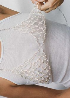 a woman is holding a piece of white fabric with pearls attached to the back of her body