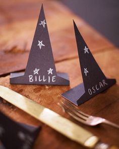 two black paper pyramids with the words billie and oscar written on them next to a knife and fork