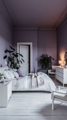 a bedroom with purple walls, white furniture and potted plants on the side table