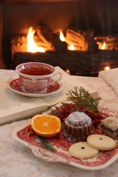 a cup of tea next to an open book and some cookies on a plate with orange slices