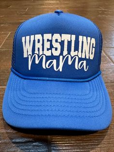 a blue wrestling mama trucker hat sitting on top of a wooden floor next to a pair of scissors