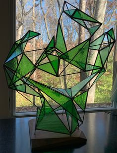 a green sculpture sitting on top of a wooden table next to a window with trees in the background