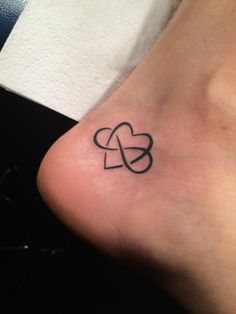 a small black heart tattoo on the side of a person's foot with an intertwined