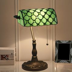 a green lamp sitting on top of a table next to a framed photo and some books