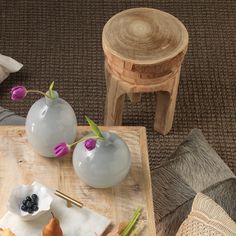 two vases with flowers are sitting on a table next to a chair and stool