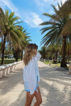 a woman walking down a sidewalk next to palm trees