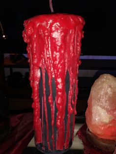 a red candle with black streaks on it next to a rock