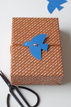 scissors are laying next to a gift wrapped in brown and white paper with blue birds on it