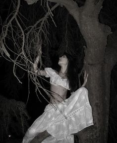 a woman is sitting in the branches of a tree at night with her arms outstretched