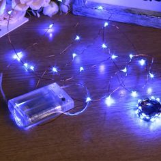 some lights that are sitting on a table next to a glass bottle and flower vase