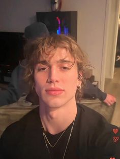 a young man with curly hair wearing a black t - shirt is looking at the camera