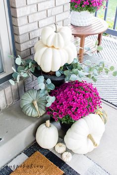 the front porch is decorated with white pumpkins and purple flowers