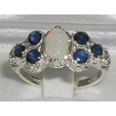 This Beautiful and Unusual Victorian Style Ring is made completely from Solid Sterling Silver and was Hallmarked in London, England.It has been hand set with a beautiful selection of Opal & Sapphires. These are genuine Opal Gemstones and a Natural Sapphires. These Colorful Vibrant Opal stand out wonderfully set against the polished Silver and contrast with the Vibrancy of the Sapphires providing such an Elegant overall appearance.The ring also boasts a well crafted Art Nouveau Style carving Opal And Sapphire Ring, Victorian Style Rings, Art Nouveau Ring, Flower Daisy, Precious Opal, Carved Ring, Daisy Ring, Sapphire Engagement Ring Blue, Pave Ring