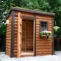 a small wooden shed with its door open and flowers hanging from the window sill