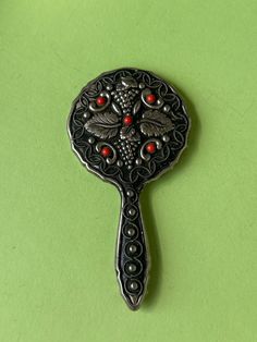 a black and silver brooch with red stones on it's face sitting on a green surface