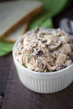 a white bowl filled with food sitting on top of a wooden table next to a slice of bread