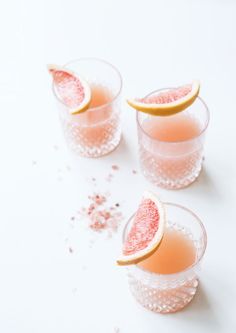 three glasses filled with grapefruit and garnish on top of a white table