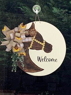 a welcome sign hanging from the side of a building with flowers in front of it