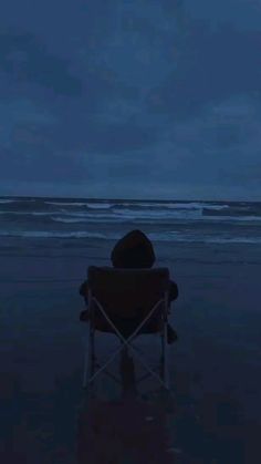 a person sitting in a chair on the beach at night