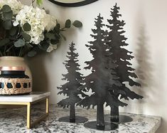 two metal trees on a marble table next to a vase with flowers and a clock