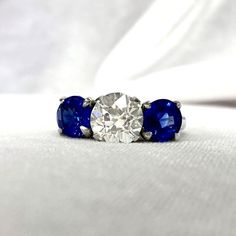 three stone diamond and blue sapphire ring on white cloth with soft background, closeup