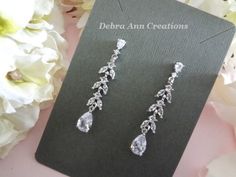 a pair of diamond earrings sitting on top of a card next to some white flowers