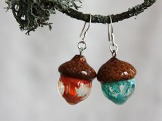 two acorns hanging from a tree branch with leaves and beads on the ear