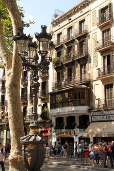 people are walking down the street in front of buildings and lamps on poles with balconies above them