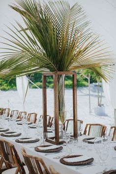 a table set up with place settings and palm tree in the centerpiece for an event