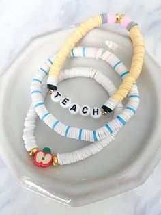 three bracelets that say teach and an apple are on top of a white plate