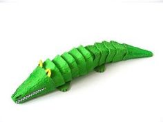 a green toy alligator with yellow eyes on it's head and tail, sitting in front of a white background