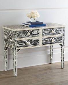 an ornate white and black dresser with flowers on it's side table next to a wall