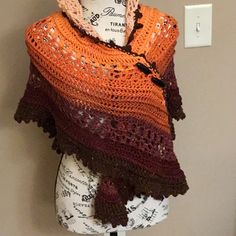 an orange and brown crocheted shawl on display