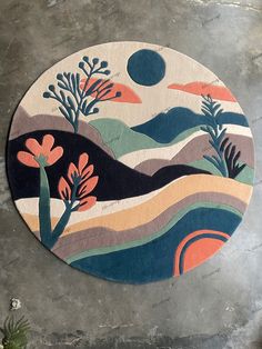 a round rug with trees and mountains painted on the floor in front of a concrete wall