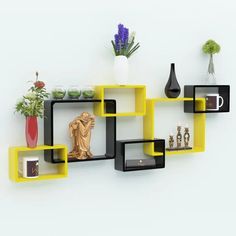 a yellow shelf with some black shelves and vases on top of it next to a white wall