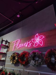 a flower shop with wreaths hanging on the wall and neon sign above it that says flowers