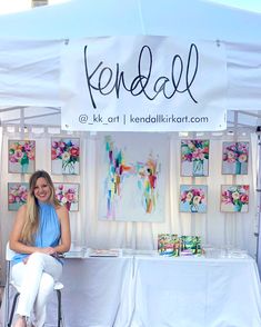 a woman sitting on a chair in front of a table with paintings and signs above it