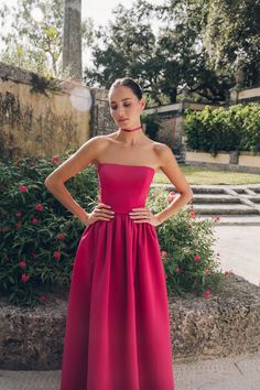 a woman in a long pink dress standing on the sidewalk with her hands on her hips