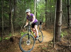 two people riding bikes on a trail in the woods