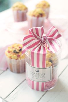 three cupcakes with pink and white stripes in a glass container on a table