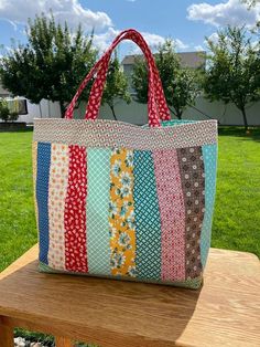 a multicolored tote bag sitting on top of a wooden bench in the grass