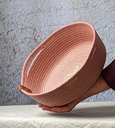 a person holding a pink basket on top of a white table next to a gray wall