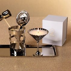 a table topped with two silver cups filled with liquid next to a candle and box