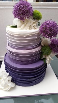 a multi layered cake with purple and white flowers