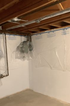 an unfinished room with white walls and exposed pipes on the wall, in which there is a plastic bag hanging from the ceiling