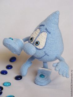 a crocheted blue toy with big eyes and arms reaching for something on the ground